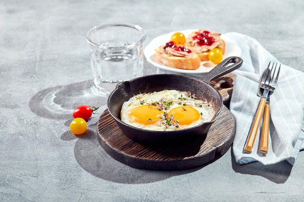 Œufs frits. Œufs frits de deux œufs dans une poêle en fonte avec tomates cerises et micropousses, pain grillé. Concept de petit-déjeuner ensoleillé