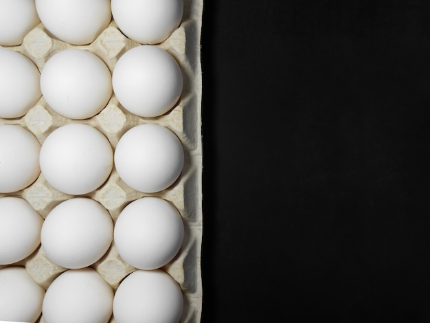 Œufs de poule crus dans une boîte à œufs sur fond noir.