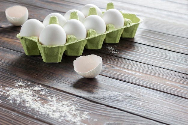 Œufs de poule dans une boîte en carton, coquille d'œuf cassée dans une plaque, fouet métallique, fond en bois foncé, espace de copie