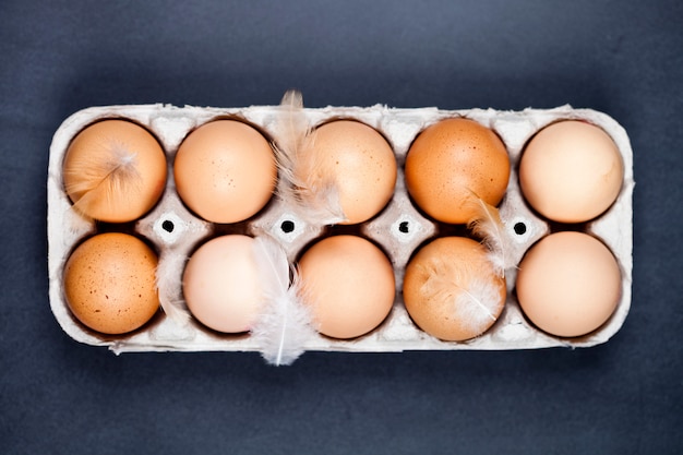 Œufs de poule de ferme dans un récipient en carton et des plumes.