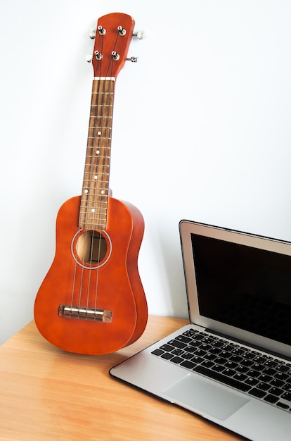 Ukulélé guitare à quatre cordes hawaïenne sur table en bois et ordinateur portable.