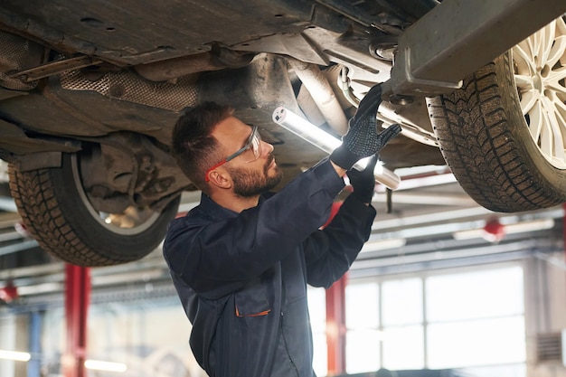 Photo en uniforme bleu, le réparateur de voiture est dans le garage avec l'automobile.