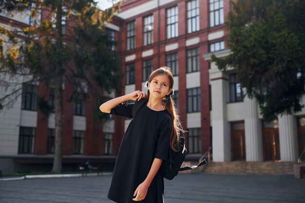 En uniforme noir, une écolière est à l'extérieur près du bâtiment de l'école