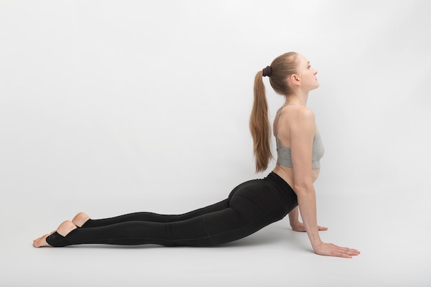 Urdhva Mukha Shvanasana, pose de chien tête en haut. Superbe fille mince vêtue d'un haut de sport blanc et de collants fait des étirements sur fond blanc.