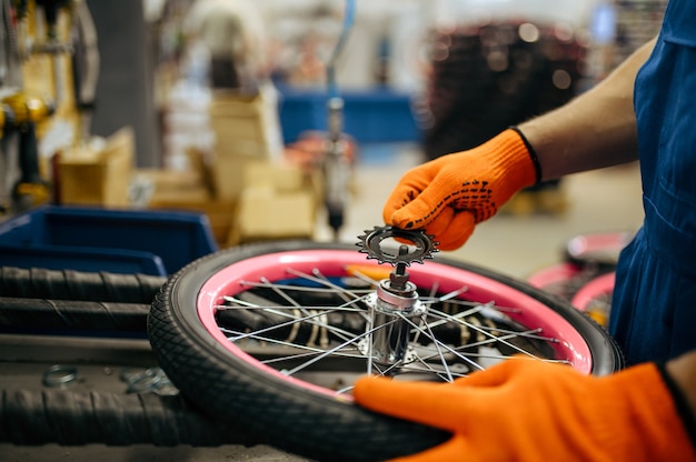 Usine de bicyclettes, le travailleur définit l'étoile sur la roue de vélo. Mâle mécanicien en uniforme installe des pièces de cycle, chaîne de montage en atelier