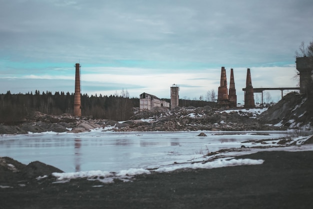 Usine détruite abandonnée devant la rivière gelée de la forêt recouverte de glace et de givre en hiver