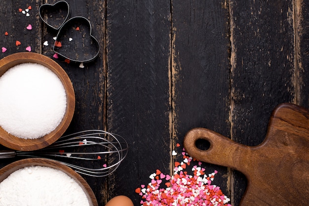 Ustensiles de cuisine, farine, cœurs et sucre sur bois