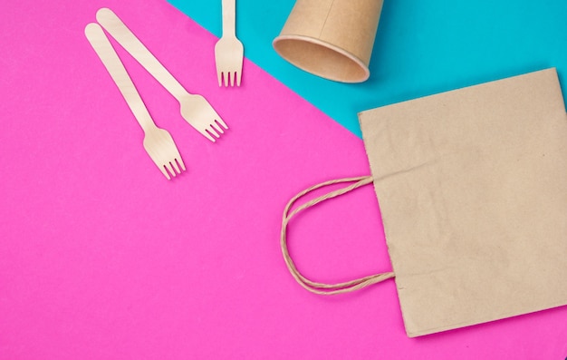 Ustensiles de cuisine jetables en matériaux naturels. Concept écologique. Fourchettes en bois, tasse à café artisanale vide, sac sur fond rose bleu. Vue de dessus