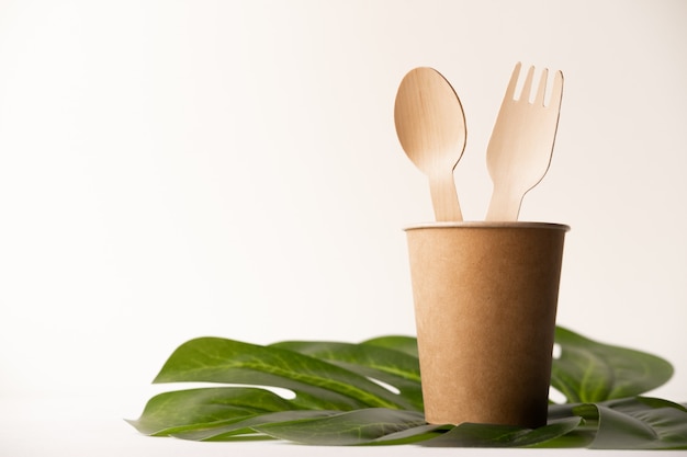 ustensiles de cuisine jetables respectueux de l'environnement sur fond blanc. fourchettes et cuillères en bois dans une tasse en papier. écologie, concept zéro déchet. vue de dessus. mise à plat