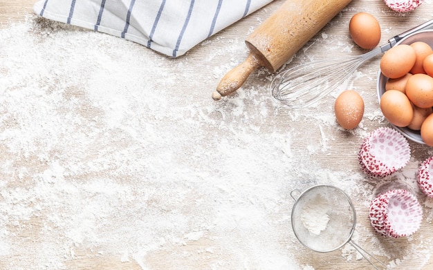 Photo ustensiles de cuisson avec de la farine d'œufs et des caissettes à cupcakes sur la table de la cuisine - haut de la vue.