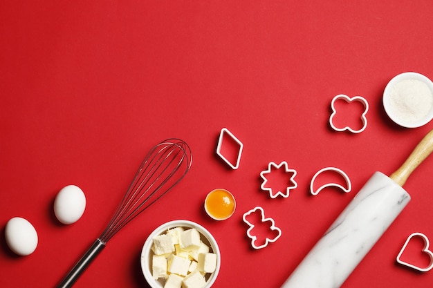 Ustensiles et ingrédients de cuisson. Rouleau à pâtisserie, saupoudrer de sucre, fouetter avec un moule à biscuits sur fond rouge. Concept de cuisson. Place pour le texte.