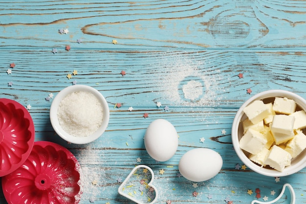 Ustensiles et ingrédients de cuisson. Ustensiles de cuisine en silicone coloré, rouleau à pâtisserie, moule à biscuits, étuis à cupcakes et saupoudrage de sucre sur un fond en bois bleu. Notion de Pâques.