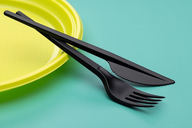 Ustensiles en plastique en gros plan. Assiette jaune jetable, couverts noirs sur fond vert vif.