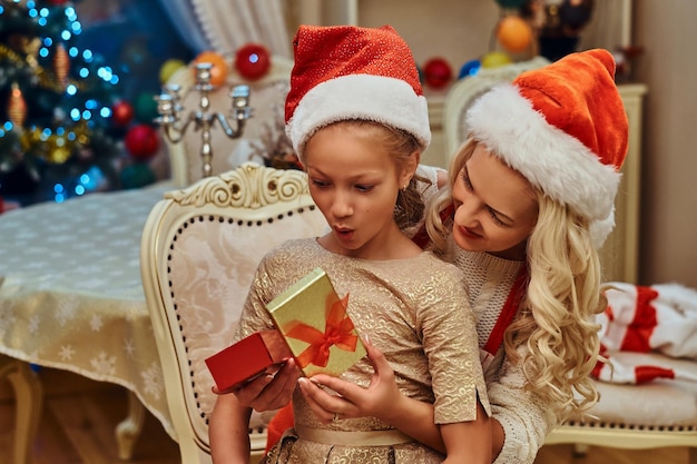 ute fille vêtue d'une belle robe est assise sur les genoux de sa mère et est surprise de son cadeau