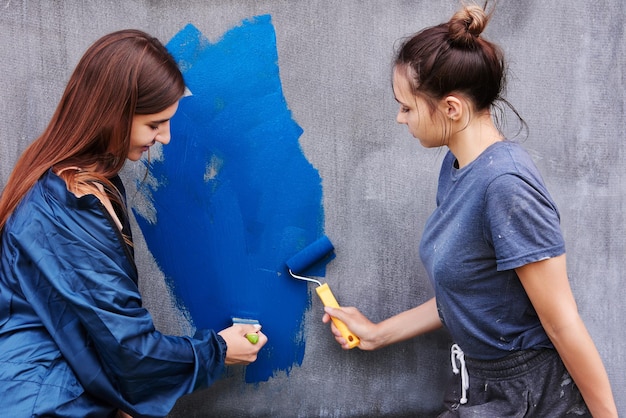 Utilisant un rouleau de peinture et un pinceau, les femmes peignent le mur gris avec de la peinture bleue.