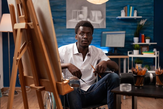 Utilisateur de fauteuil roulant de dessinateur afro-américain travaillant dans un studio d'art. Dessinateur professionnel vivant avec une mobilité réduite utilisant des stylos et un chevalet pour créer des œuvres d'art.