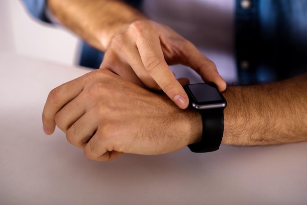 Utilisateur moderne Gros plan d'un homme agréable utilisant sa montre-bracelet intelligente tout en se tenant près de la table