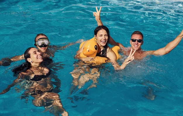 Utilisation d'un canard de couleur jaune pour nager Un groupe de jeunes gens heureux s'amuse dans la piscine pendant la journée