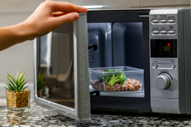 Utilisation du four à micro-ondes pour chauffer des aliments. Récipient en plastique chauffant avec du brocoli et du sarrasin au micro-ondes