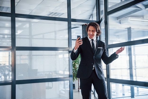 Utilisation du téléphone. Portrait de beau jeune homme d'affaires en costume noir et cravate.