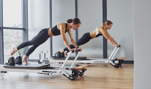 Utilisation de l'équipement de gym Deux femmes en vêtements de sport et aux corps minces ont ensemble une journée de yoga à l'intérieur