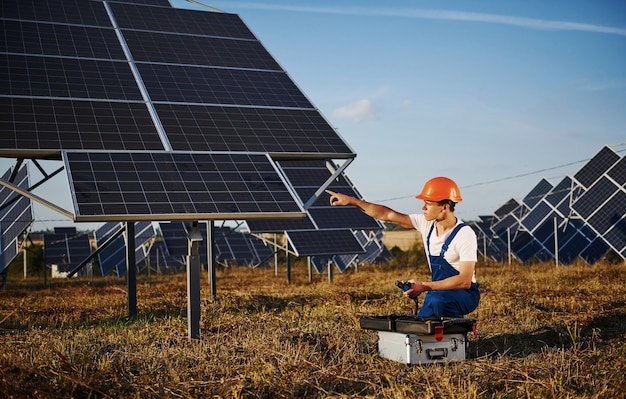 Utilisation d'équipements spéciaux. Travailleur masculin en uniforme bleu à l'extérieur avec des batteries solaires aux beaux jours.