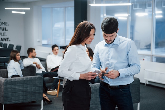 Utilisation de smartphones. Deux employés de bureau en vêtements classiques parler devant des employés