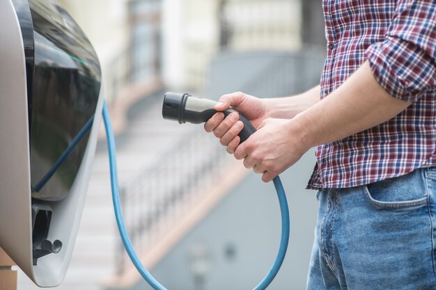 Utilisation, station de charge. Mains fortes mâles tenant le câble de la station de charge à l'extérieur, pas de visage