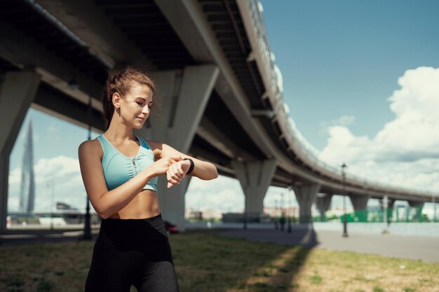 Utilise une montre intelligente athlétique femme confiante entraînement en plein air actif course et échauffement du corps