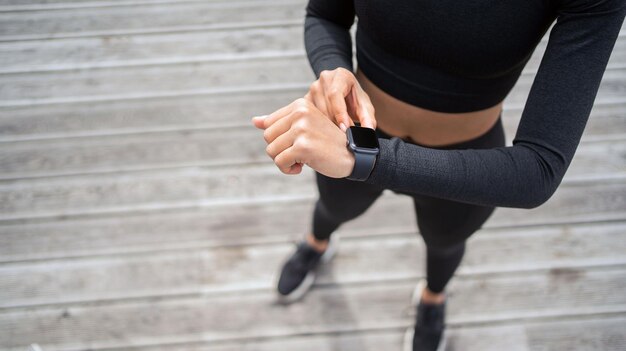 Utilise une smartwatch avec un pouls et une machine cardio une entraîneuse s'entraîne à l'extérieur en vêtements de sport