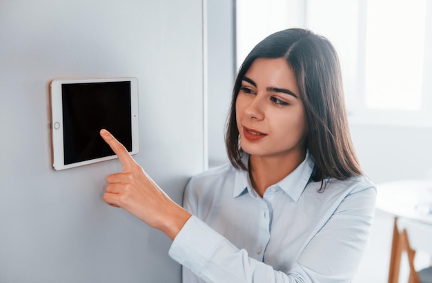 Utilise une tablette fixée au mur La jeune femme est à l'intérieur dans la chambre de la maison intelligente pendant la journée