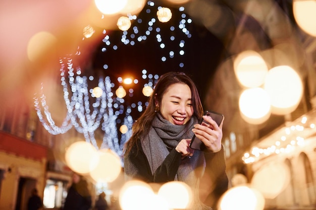 Utilise le téléphone Une jeune femme asiatique mignonne et heureuse à l'extérieur de la ville célèbre le nouvel an