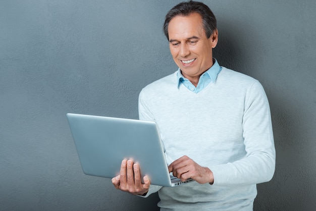 Utiliser la technologie pour un grand avantage. Homme mûr gai travaillant sur l'ordinateur portable et souriant