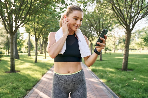 Utilisez la technologie joyeuse femme en tenue de sport et des écouteurs sans fil à l'aide de son smartphone tout en