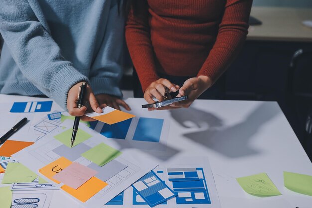 UX UI designer testing prototype on a phone discussing and brainstorming on wireframes for a website and mobile app prototype in the concept of website and mobile application design concept