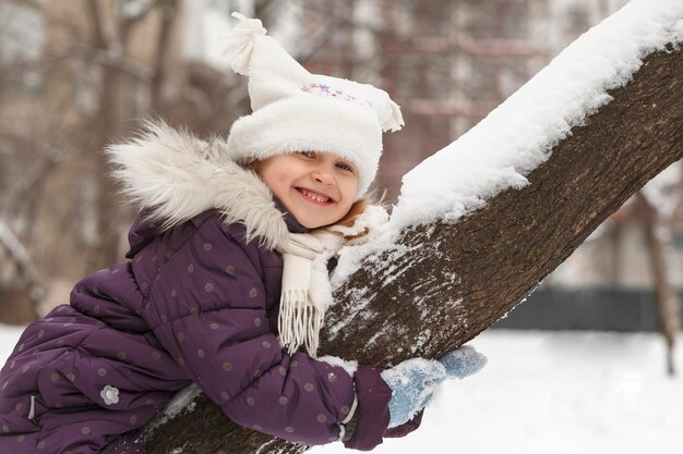 Vacances d'activités d'hiver La fille drôle est heureuse sur l'arbre enneigé Sourire portrait positif en hiver