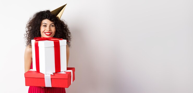 Photo vacances et célébration belle dame aux cheveux bouclés portant un chapeau de fête et tenant de gros cadeaux s