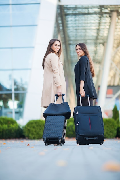 Vacances. Deux filles heureuse voyageant à l'étranger ensemble, transportant une valise à l'aéroport