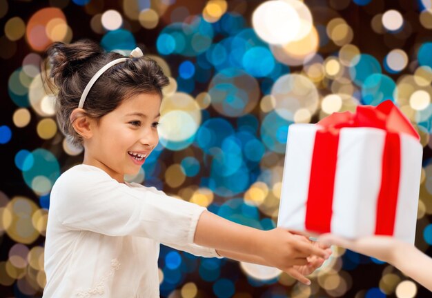 Photo vacances, enfance et concept de personnes - petite fille souriante donnant ou recevant un cadeau sur le fond des lumières