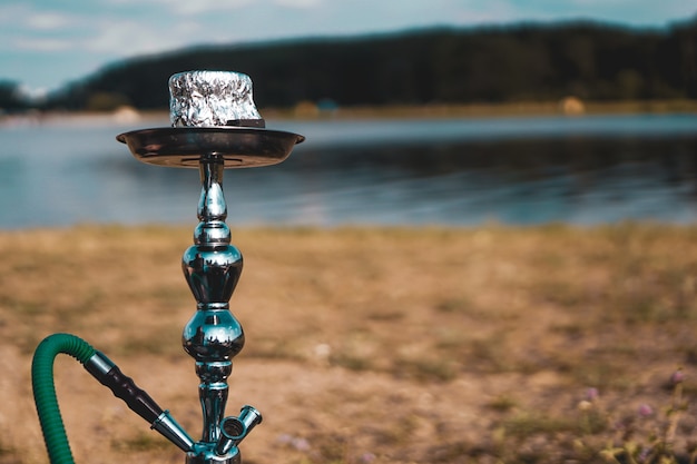 Vacances d'été, activité. environnement, voyage et concept de fumer le narguilé. Le bol de narguilé se trouve dans la nature au bord de la rivière en gros plan