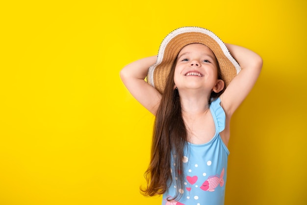 Vacances d'été au bord de la mer Portrait d'une jeune fille joyeuse en maillot de bain bleu et chapeau fond jaune