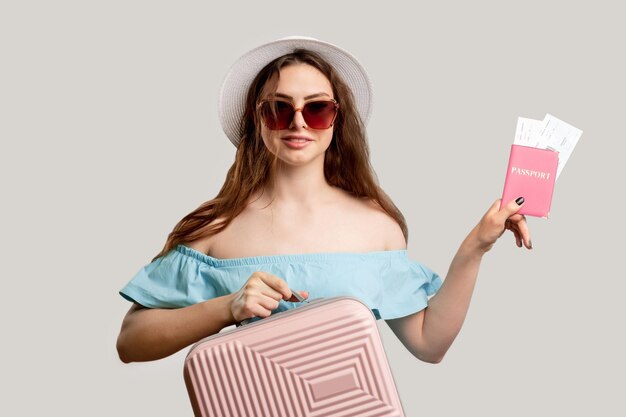 Vacances d'été Enregistrement de vol Heureuse femme en tenue de vacances tenant une valise rose et une carte d'embarquement pour carte d'identité étrangère Regardant la caméra isolée sur neutre Contrôle des passeports Heure de départ