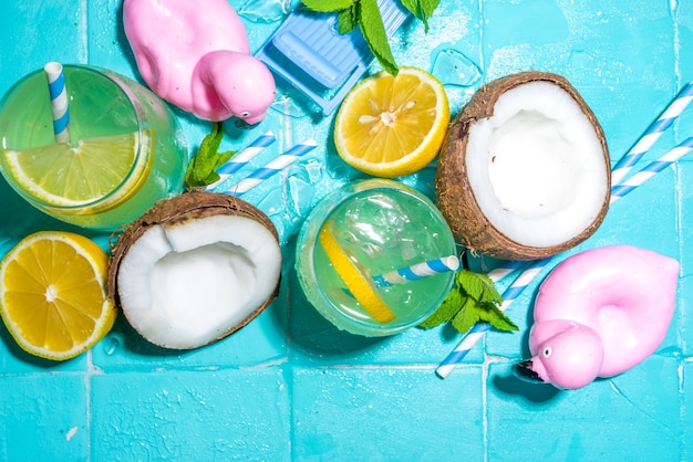 Vacances d'été ensoleillées et lumineuses. Boisson à la limonade sur fond de carreaux de piscine bleus humides, avec accessoires de vacances à la plage, bouées de sauvetage flamants roses, citrons, noix de coco, menthe, feuilles tropicales, espace de copie vue de dessus flatlay