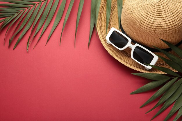 Vacances d'été mise à plat Feuilles de palmier chapeau de paille et lunettes de soleil sur fond rouge Copier l'espace