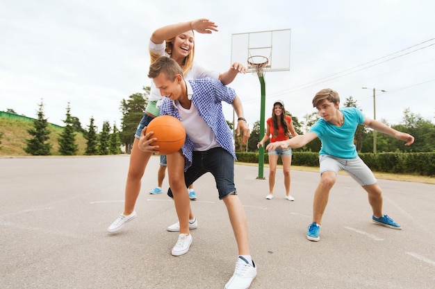vacances d'été, sport, jeux et concept d'amitié - groupe d'adolescents heureux jouant au basket à l'extérieur