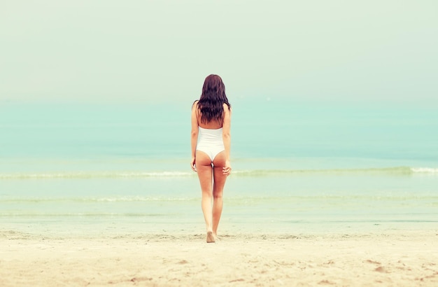 vacances d'été, tourisme, voyage, vacances et concept de personnes - jeune femme en maillot de bain marchant sur la plage de dos