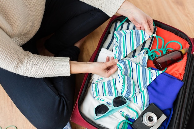 vacances d'été, voyage, tourisme et concept d'objets - gros plan d'une femme emballant un sac de voyage pour les vacances