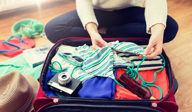 vacances d'été, voyage, tourisme et concept d'objets - gros plan d'une femme emballant un sac de voyage pour les vacances