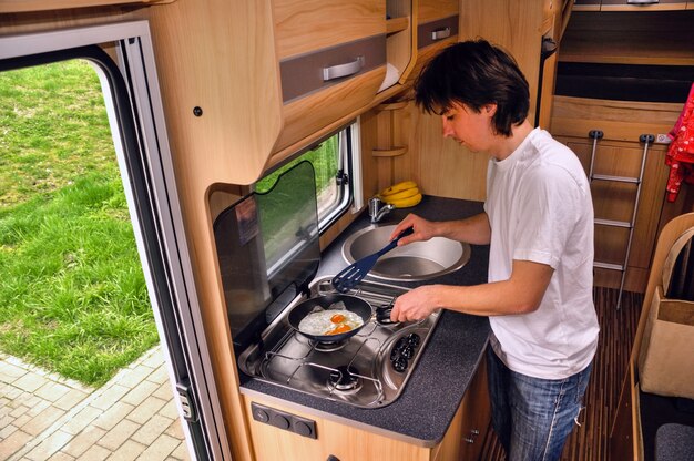 Vacances en famille, voyage de vacances RV, homme cuisine en camping-car. Intérieur camping-car