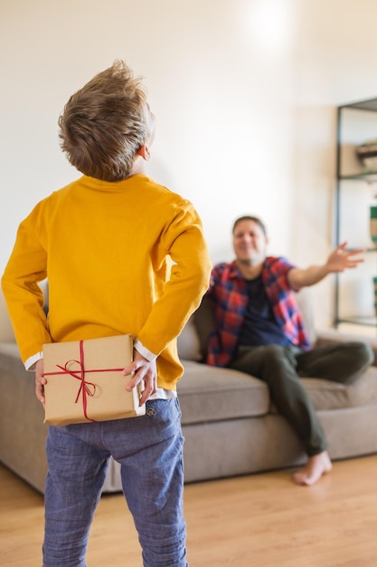 Vacances de la fête des pères. Un jeune garçon mignon donne une boîte-cadeau faite à la main à son père. Famille heureuse, temps ensemble, restez à la maison.